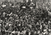 A black and white image of a crowd of people, the Chilean flag can be seen waving